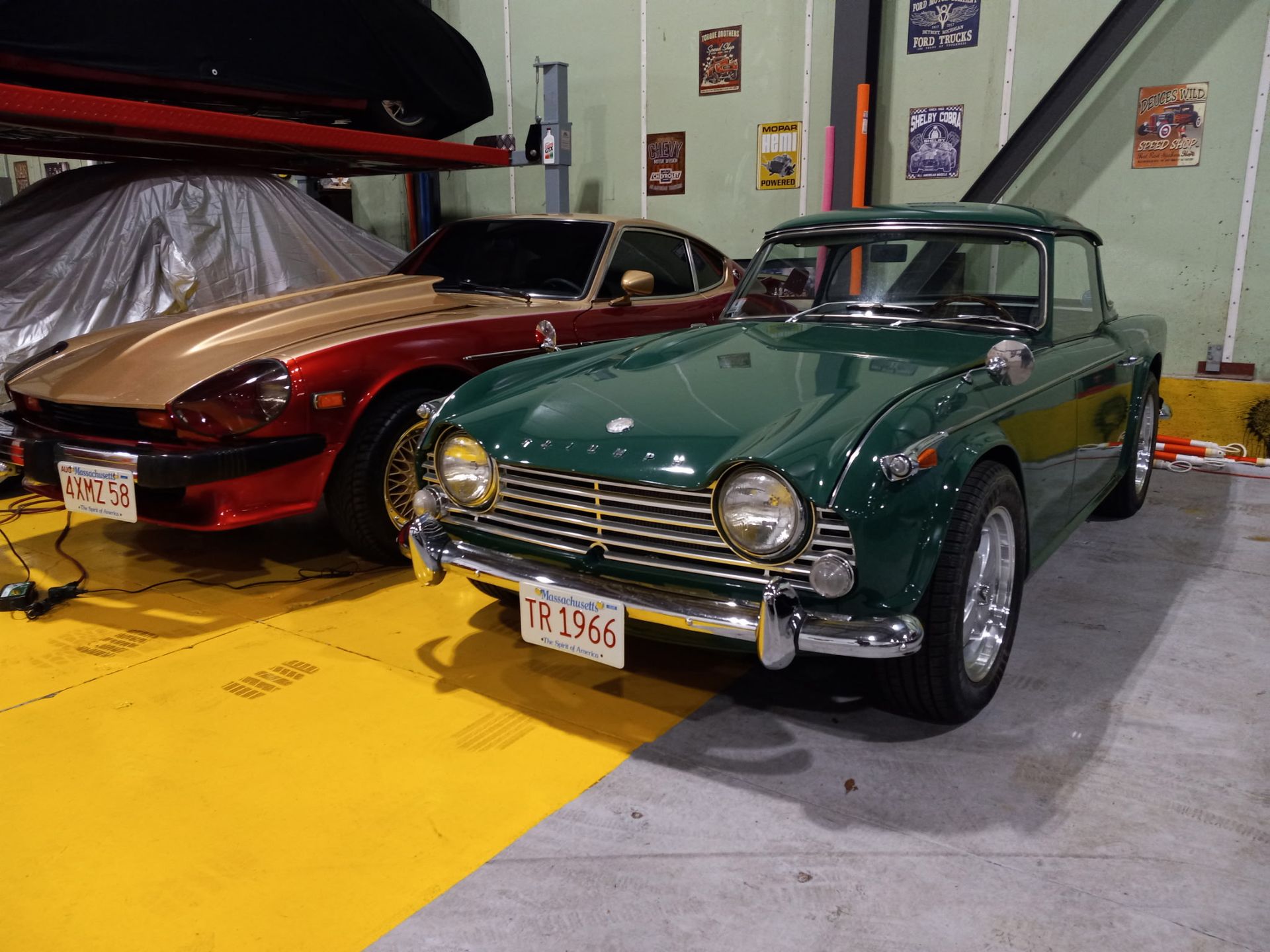Two classic cars parked indoors, including a green vintage coupe in the foreground.