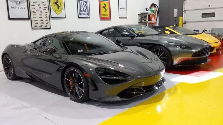 Two gray sports cars and a yellow car displayed in a showroom with framed wall art.