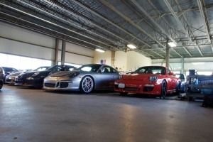 Sports cars parked inside a warehouse-like garage, including a silver coupe and a red convertible.