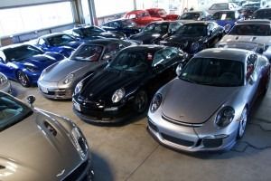 Row of sports cars parked indoors in a showroom, including black, silver, red, and blue vehicles