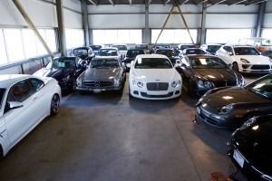 Indoor car lot filled with luxury cars, including white, black, and brown vehicles parked in rows.
