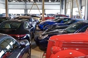 Indoor parking lot filled with parked cars in red, black, and blue under a metal roof.