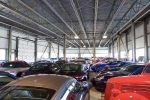 Cars packed inside a large indoor showroom with a metal roof and tall windows.