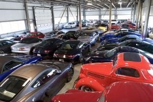 Indoor warehouse filled with rows of parked sports cars in red, black, blue, and silver