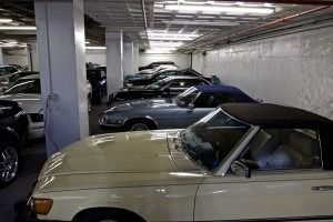 Parking garage with several parked cars, including a cream convertible in the foreground.