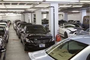 Indoor parking garage filled with parked cars, including a black Mercedes in the center foreground