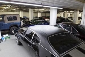 Parking garage with several cars, including a black classic coupe in the foreground.
