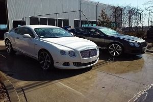 Two parked luxury sedans, one white and one black, beside an industrial building.