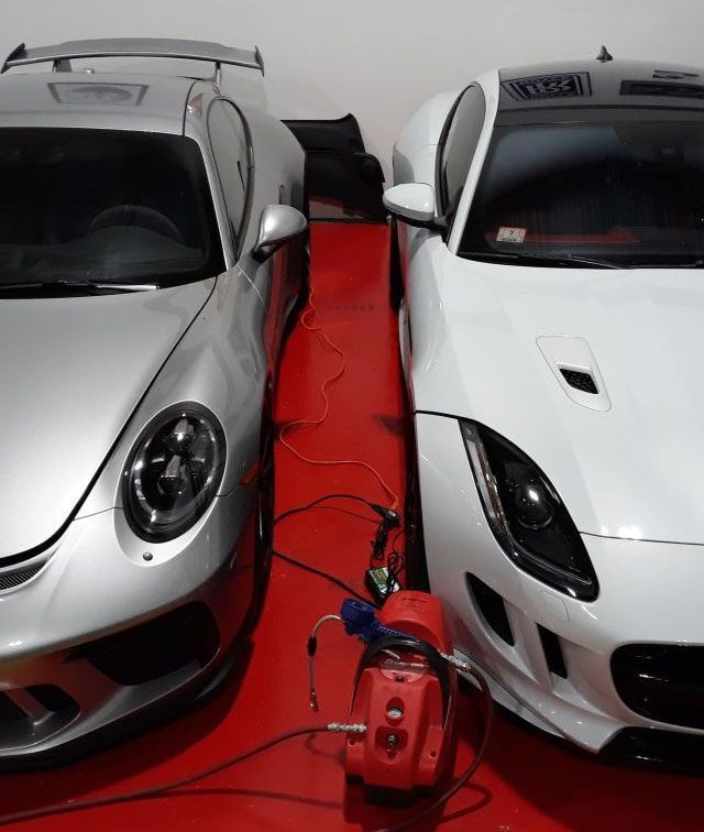 Two white sports cars parked closely with a red carpet and a red vacuum cleaner between them.