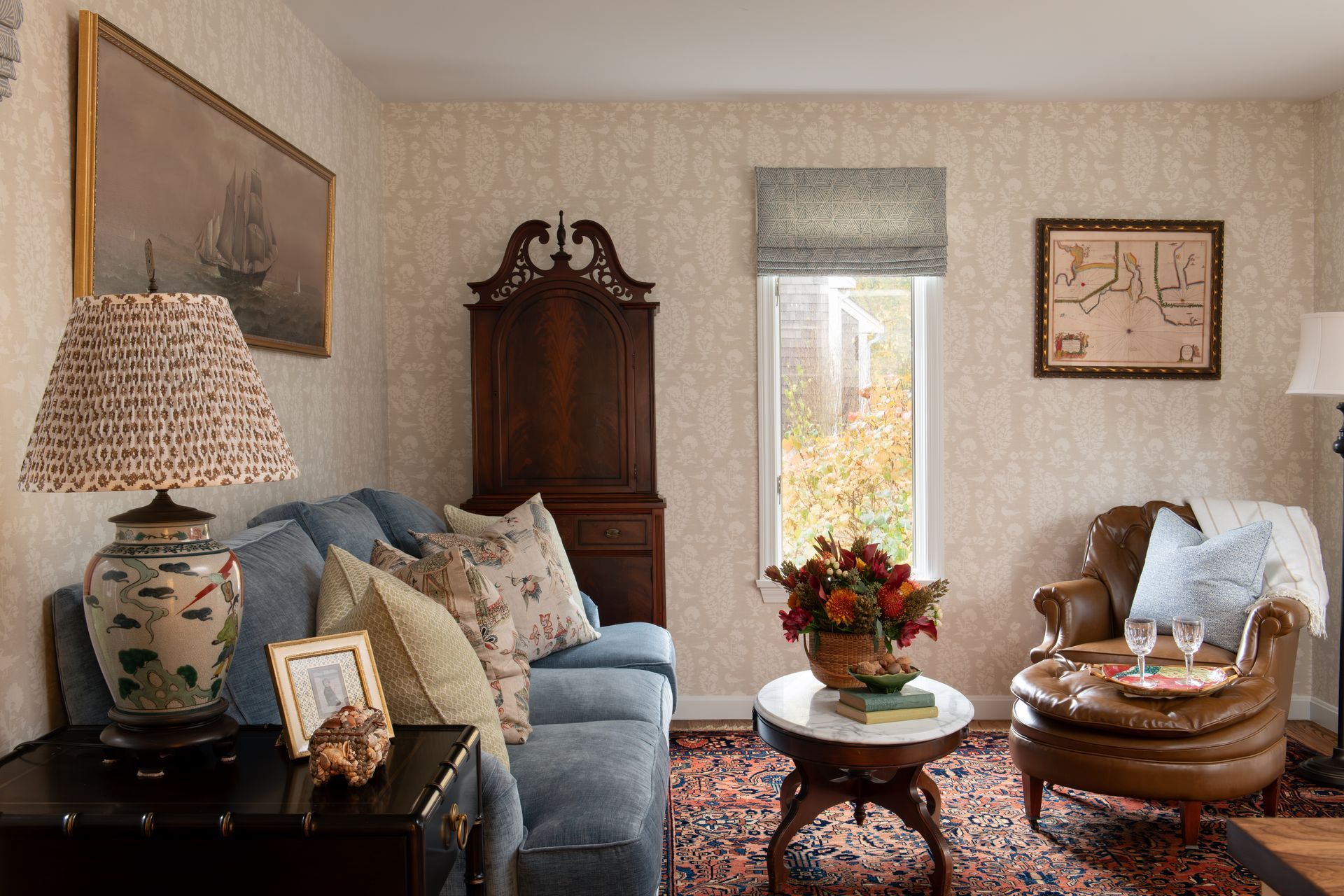 Living room with blue sofa, leather armchair, antique furniture, floral rug, and window.