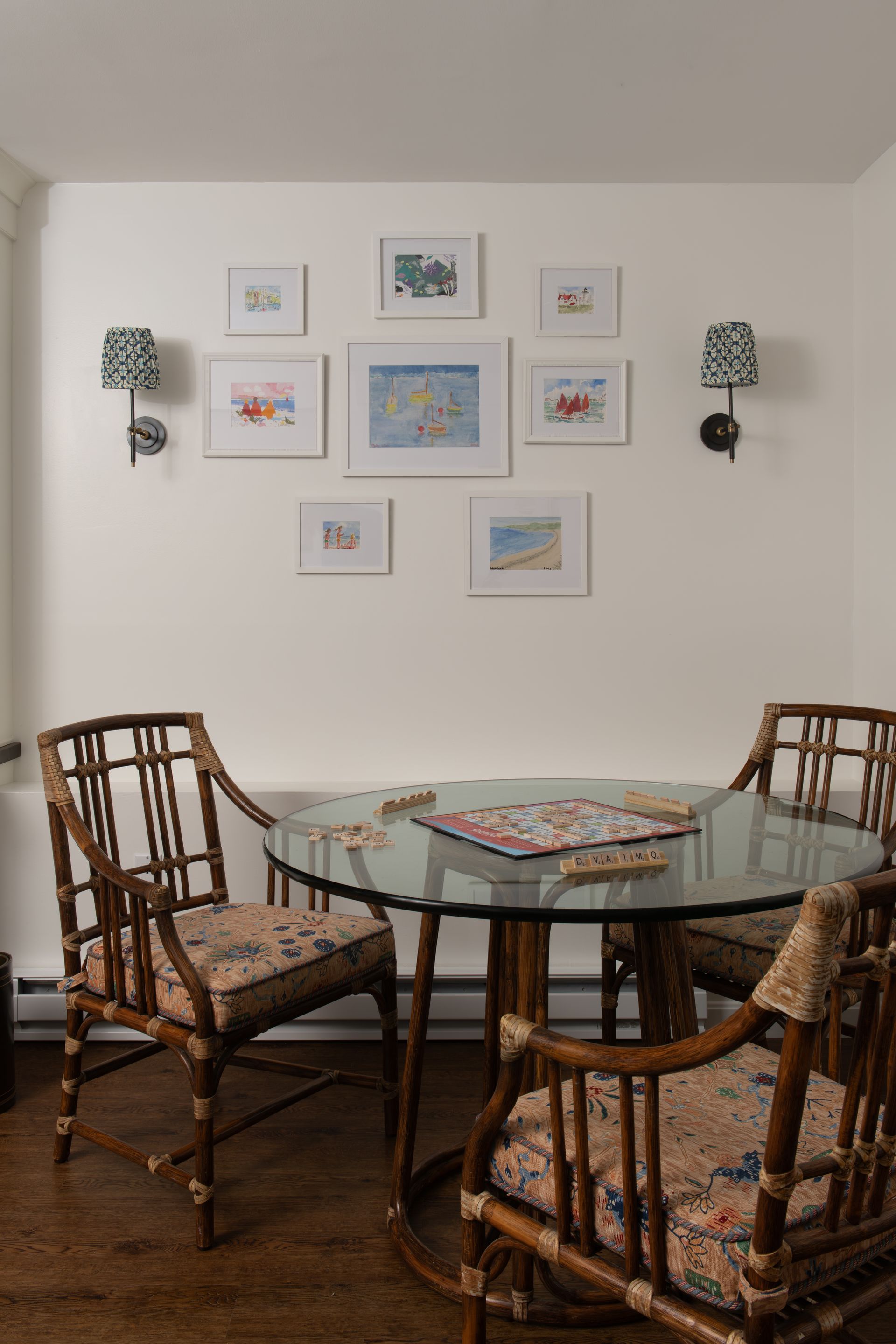 A dining area with a round glass table and four bamboo chairs. Artwork hangs on the wall.