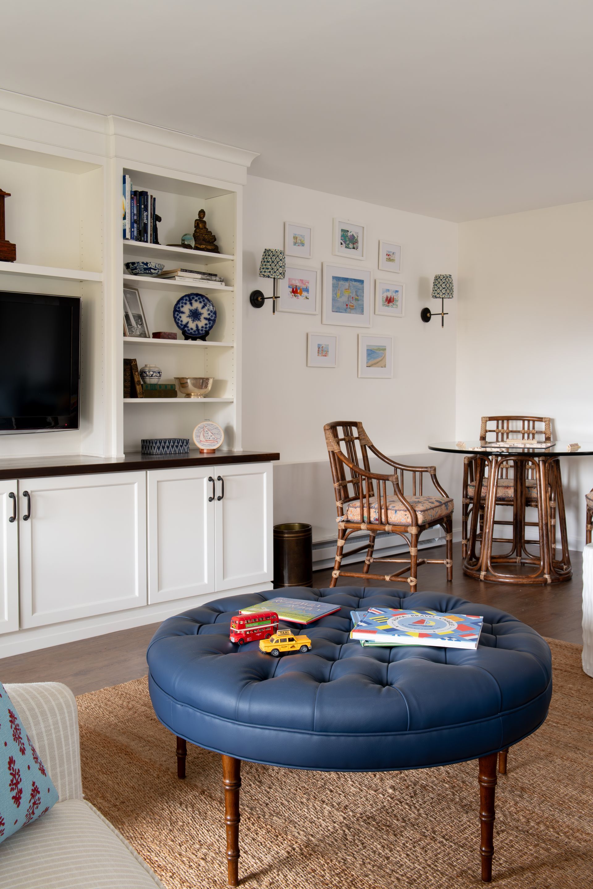 Blue ottoman in living room with built-in shelves and framed art. Toys and books are on the ottoman.