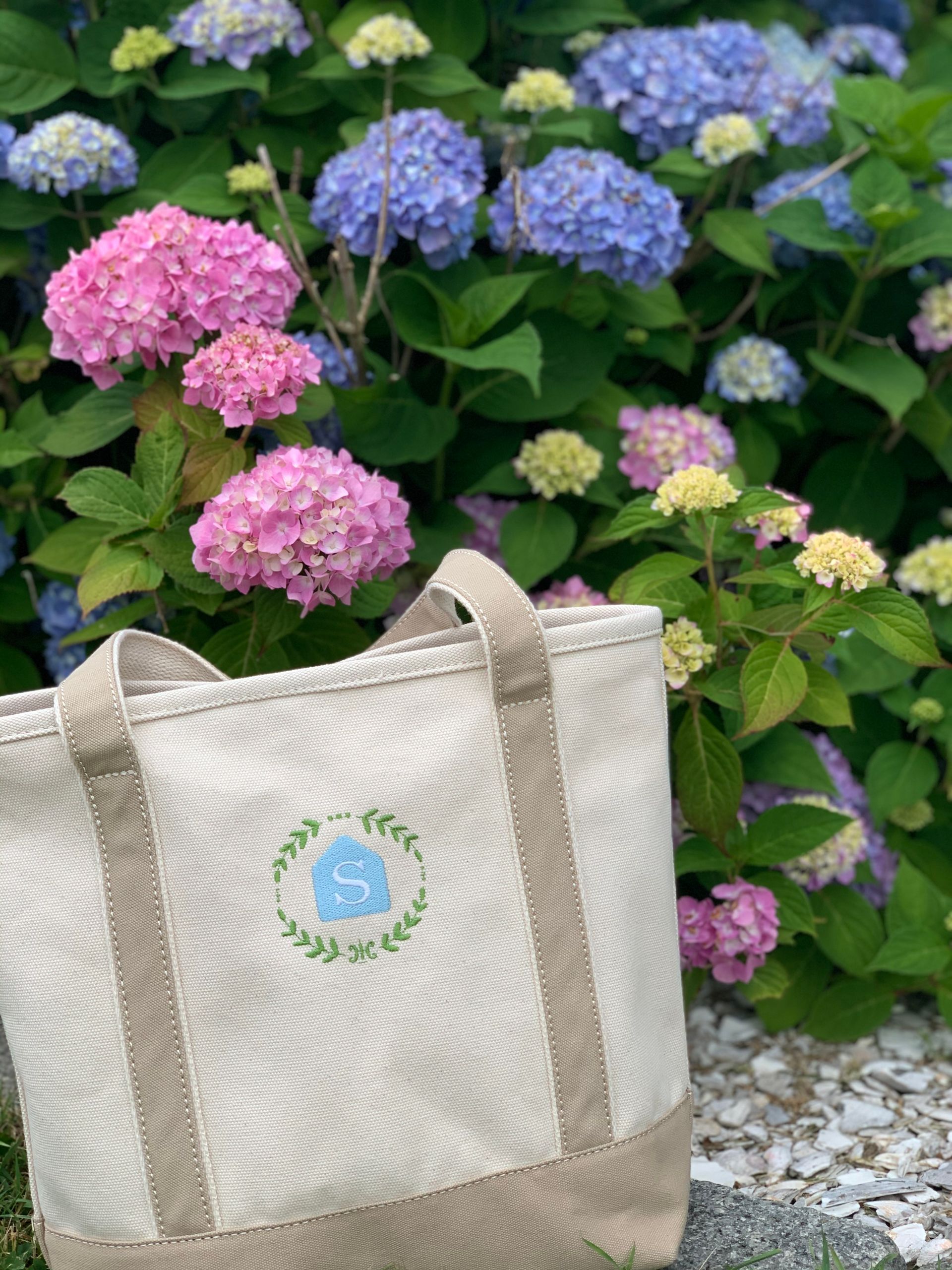 Canvas tote bag with a house logo in front of pink and blue hydrangeas.