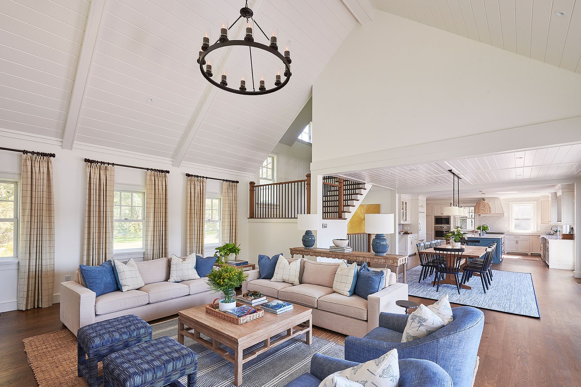 Living room with white vaulted ceiling, blue accents, open to kitchen and dining area.