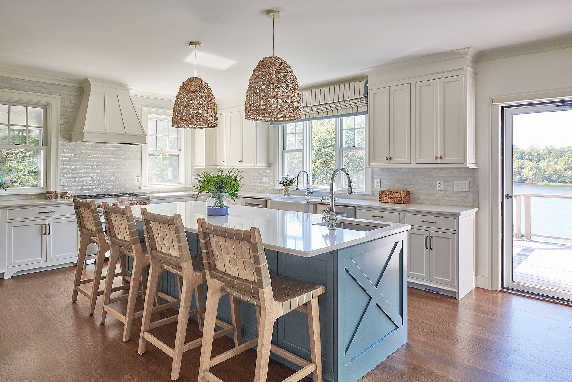 Spacious kitchen with blue island, white cabinets, and woven pendant lights. Bar stools line the island.