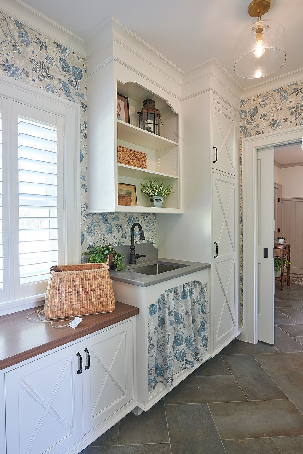 Laundry room with white cabinetry, floral wallpaper, and a sink.