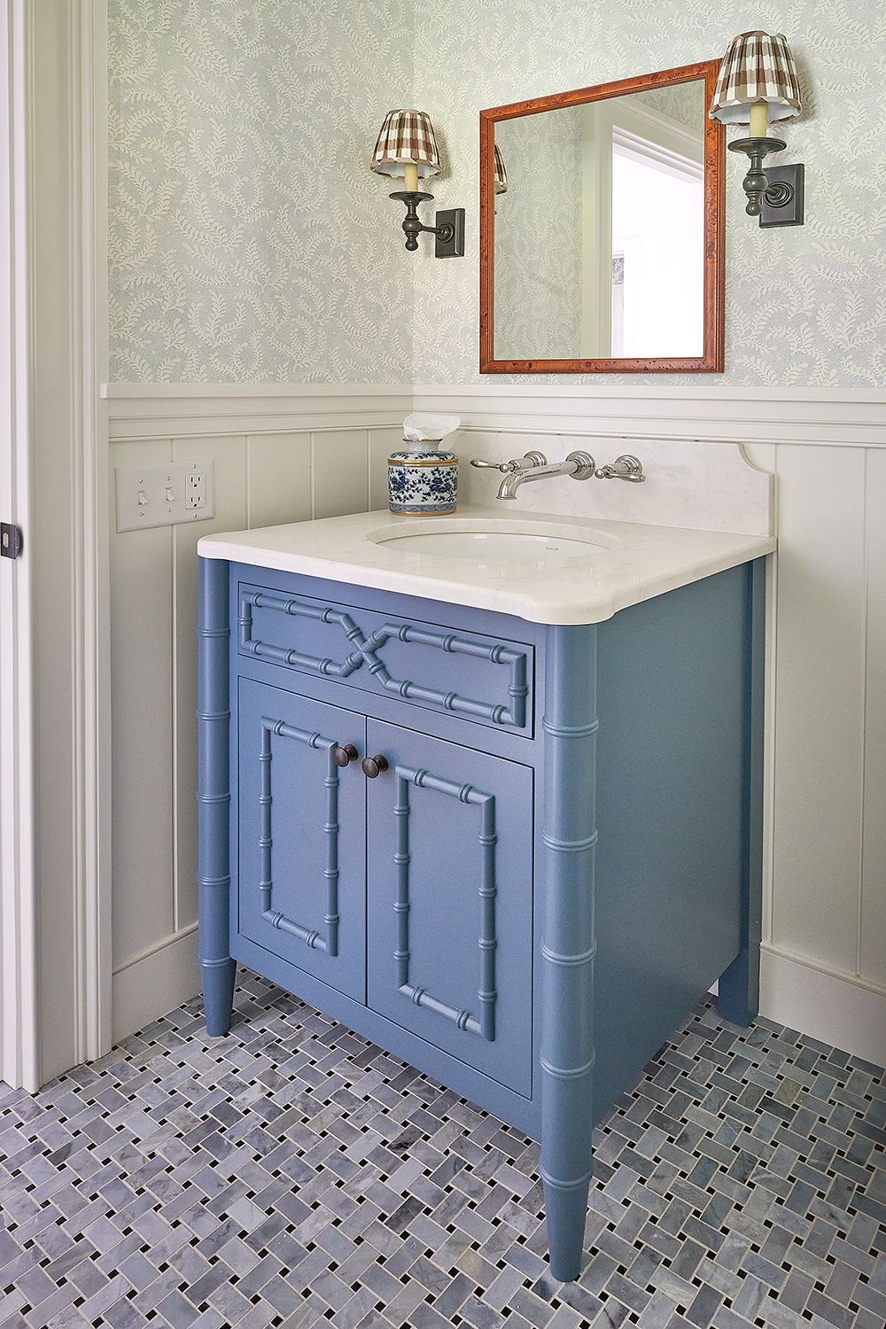 Blue bathroom vanity with white countertop, square mirror, floral wallpaper, and patterned tile floor.