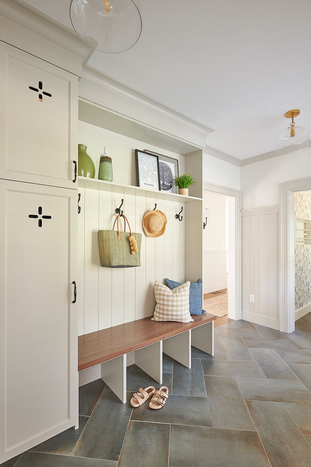 A well-organized entryway with a built-in bench, storage, and hooks, with stone flooring and white cabinets.