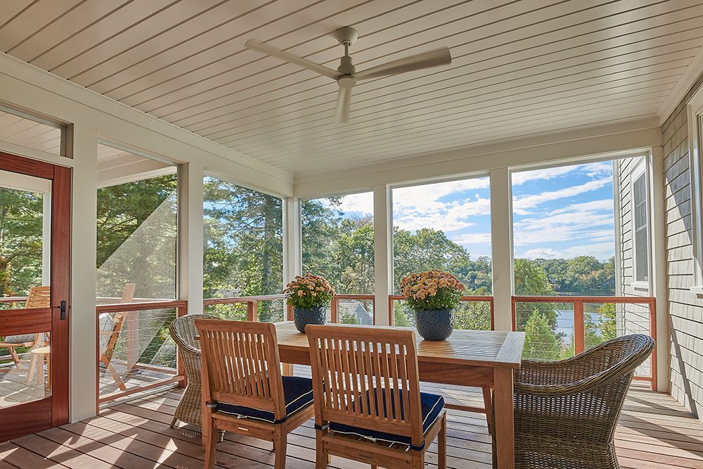 Screened-in porch with wooden table, chairs, and view of trees and water. Ceiling fan present.