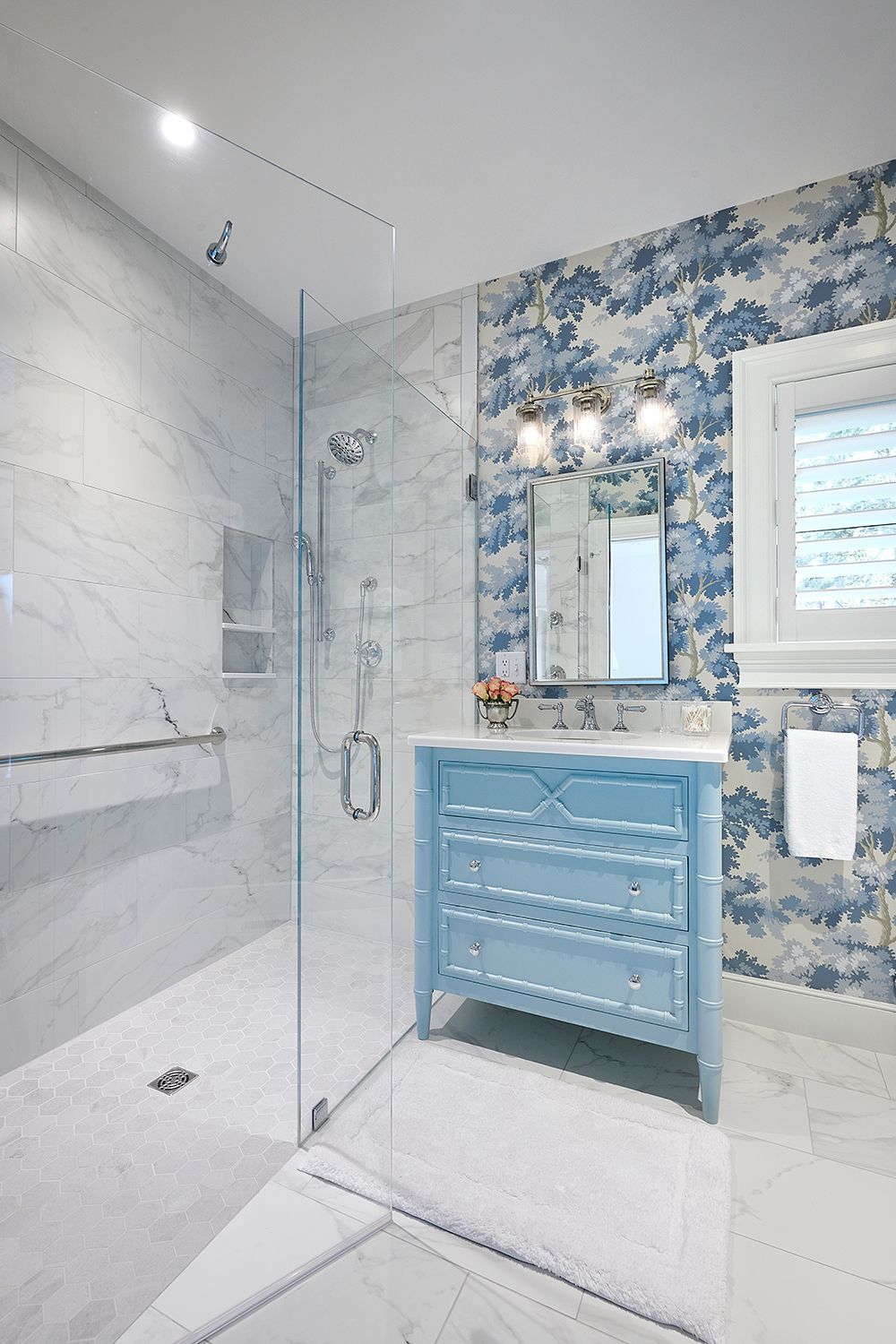 Blue and white bathroom with marble shower, vanity, and floral wallpaper.