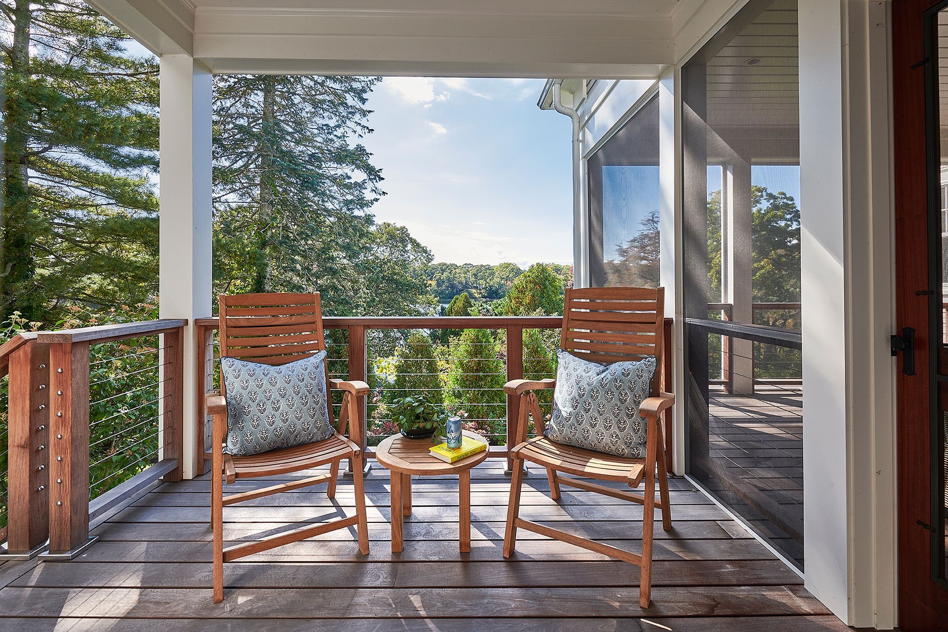 Wooden chairs on porch overlooking lush trees and a blue sky.