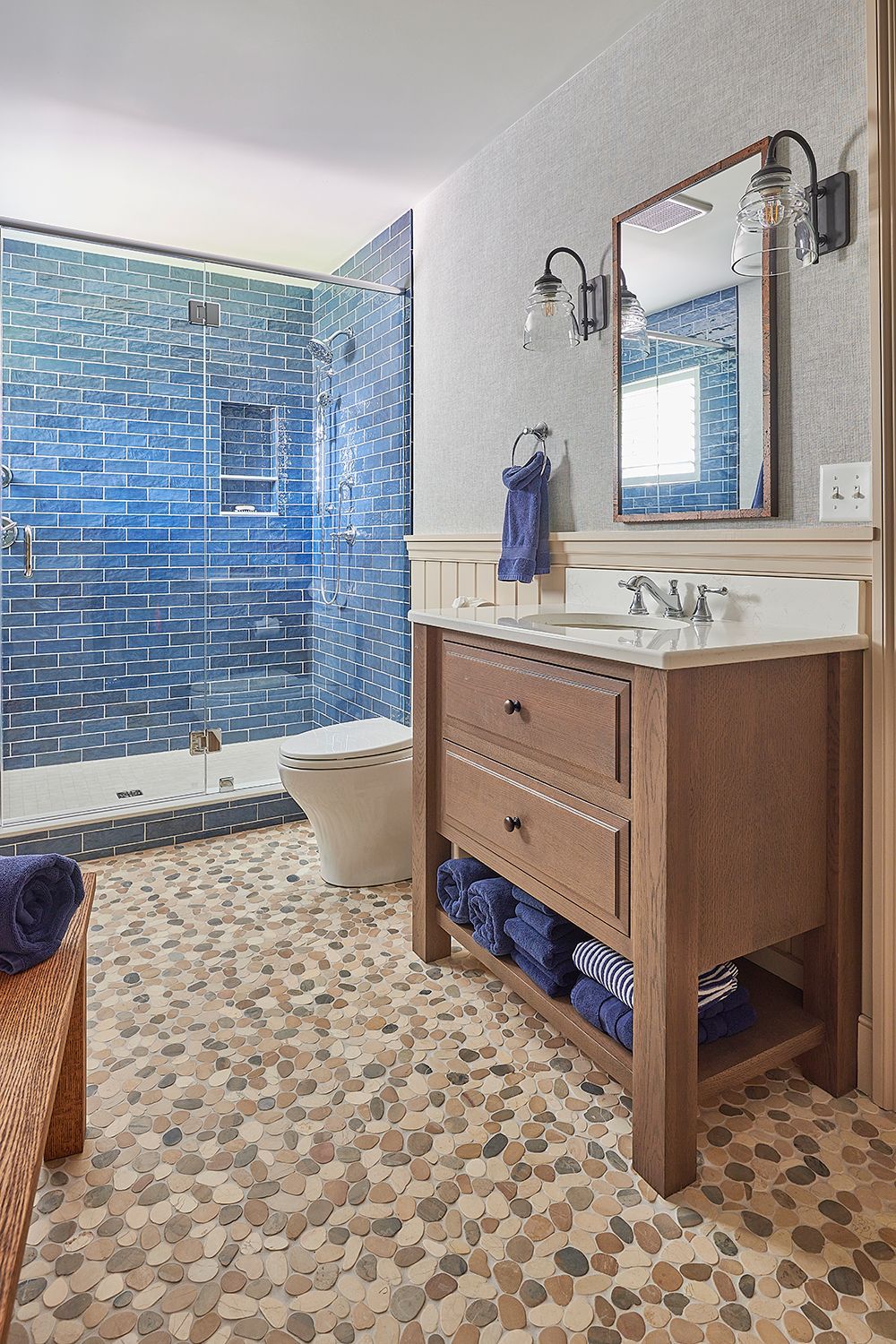 Blue tiled bathroom with pebble floor, wooden vanity, and shower.