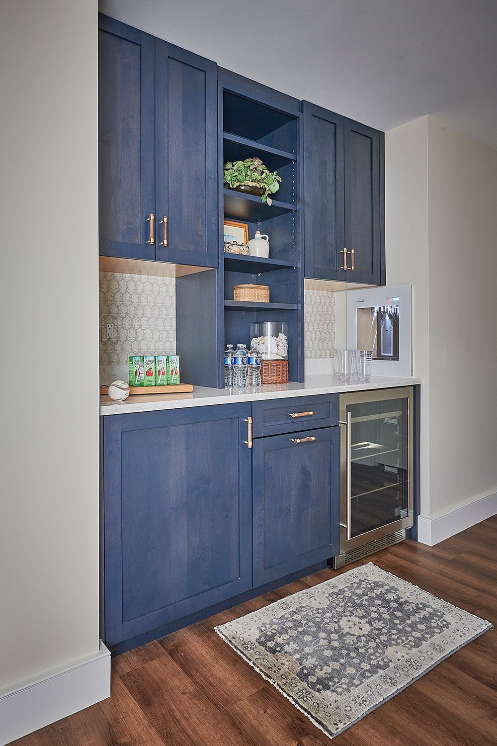 Blue cabinets form a built-in bar area. A mini-fridge sits below, and a decorative rug is on the wooden floor.