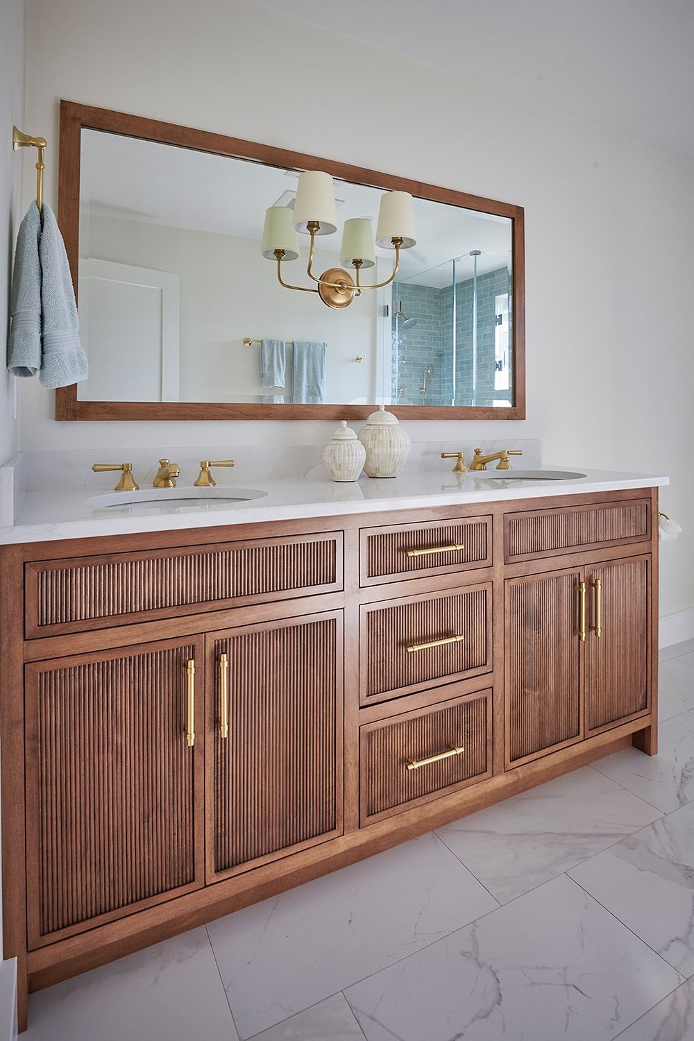 Bathroom vanity with wood cabinetry, marble countertop, and gold fixtures. Large mirror with light fixture.