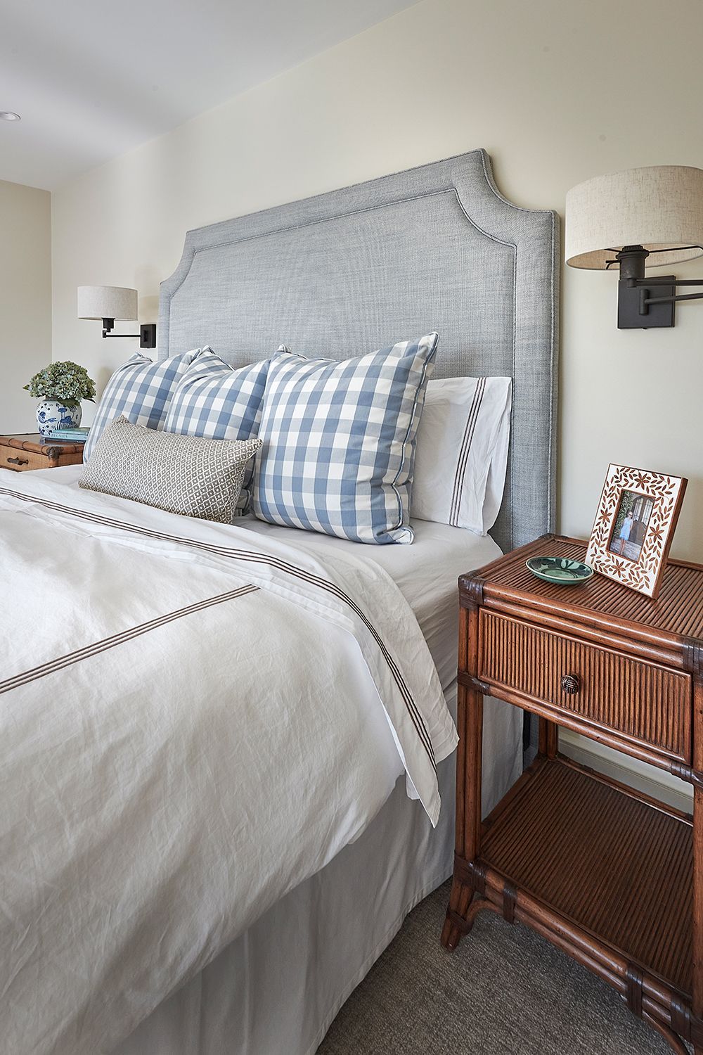 Bedroom with a gray headboard, blue and white pillows, white bedding, and a rattan nightstand.