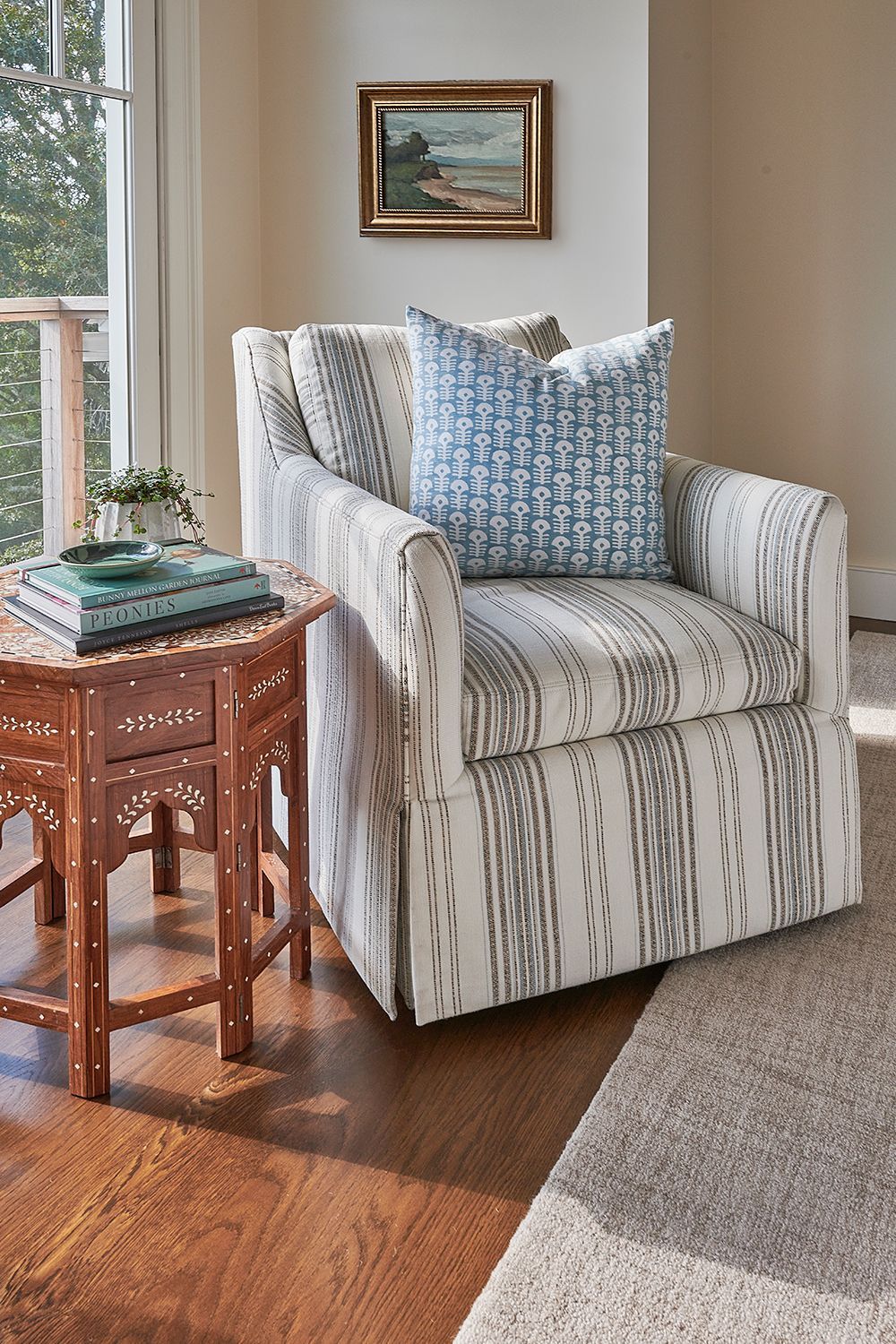 Chair with striped fabric, blue pillow, next to a carved wooden side table in a sunny room.