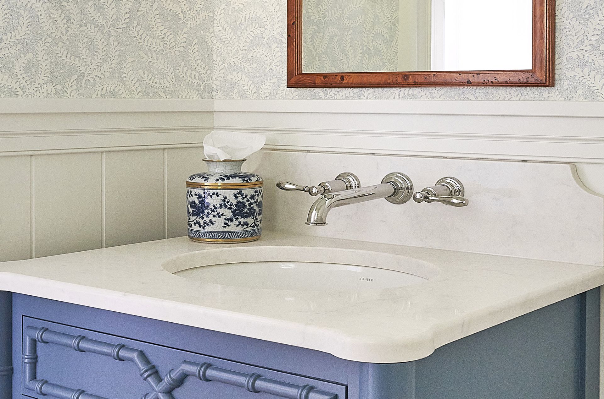 Blue vanity with marble countertop and wall-mounted faucet; blue and white tissue holder.