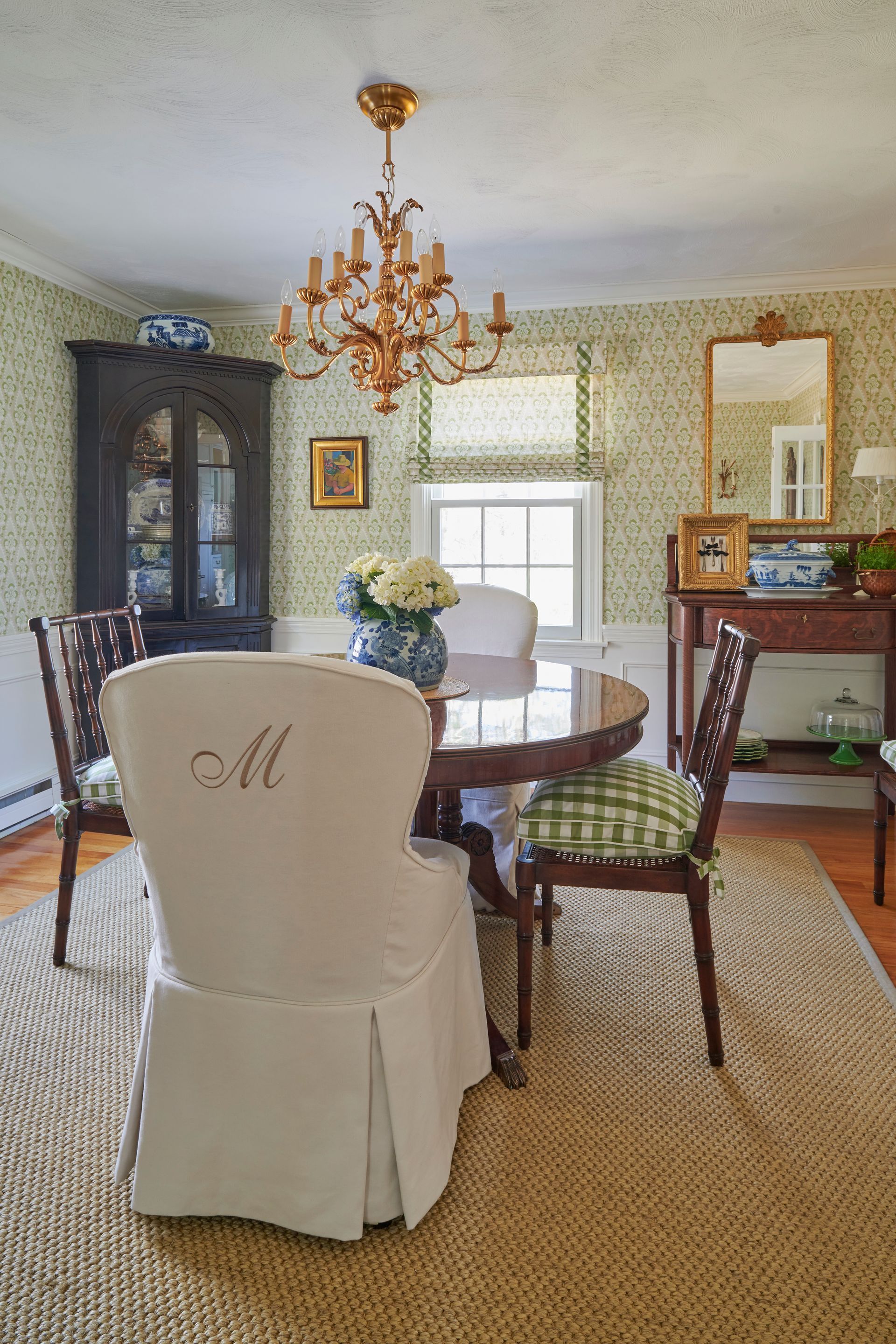 Dining room with round table, chairs, chandelier, and floral wallpaper.
