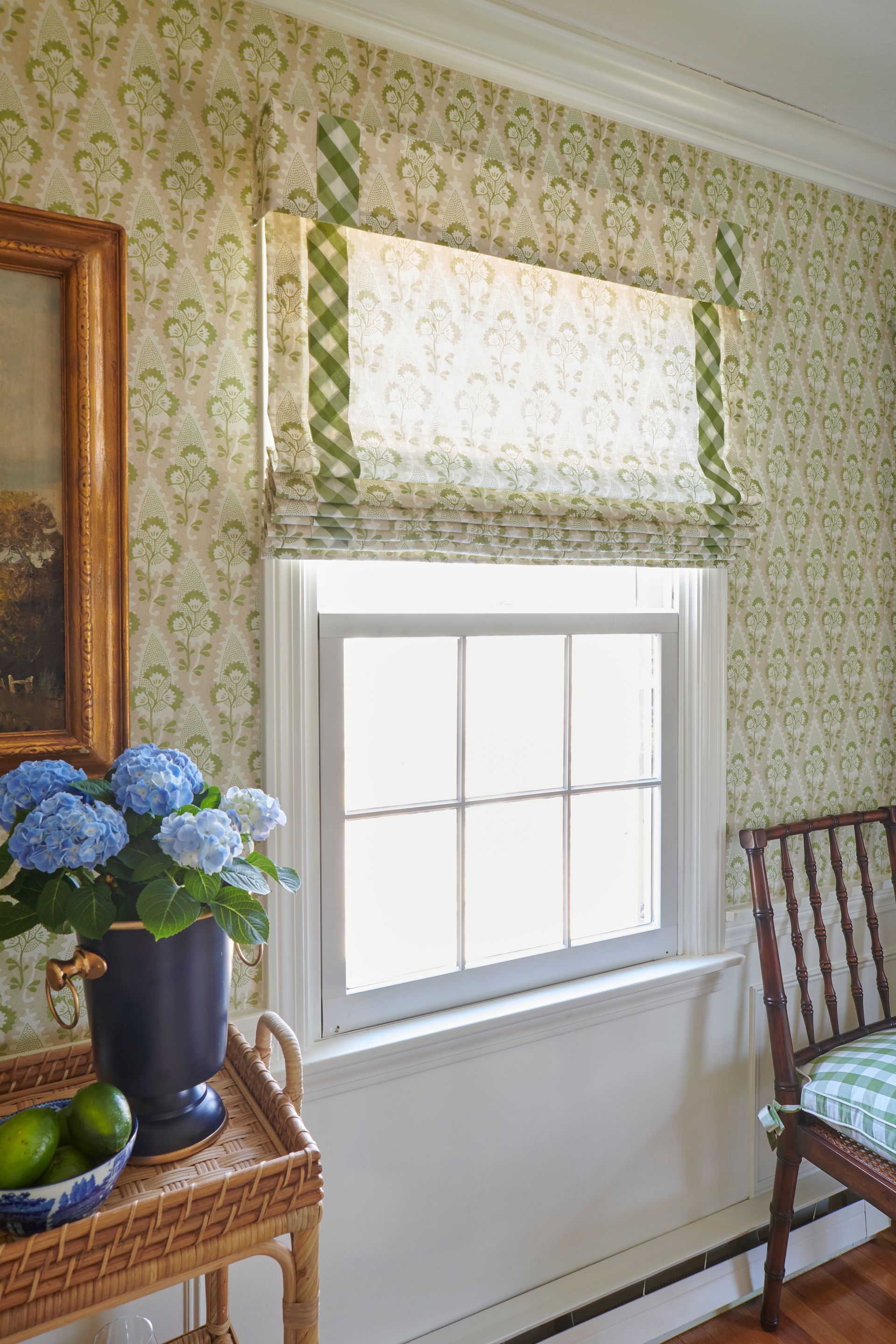 Window with patterned wallpaper, blue hydrangeas, and a roman shade.