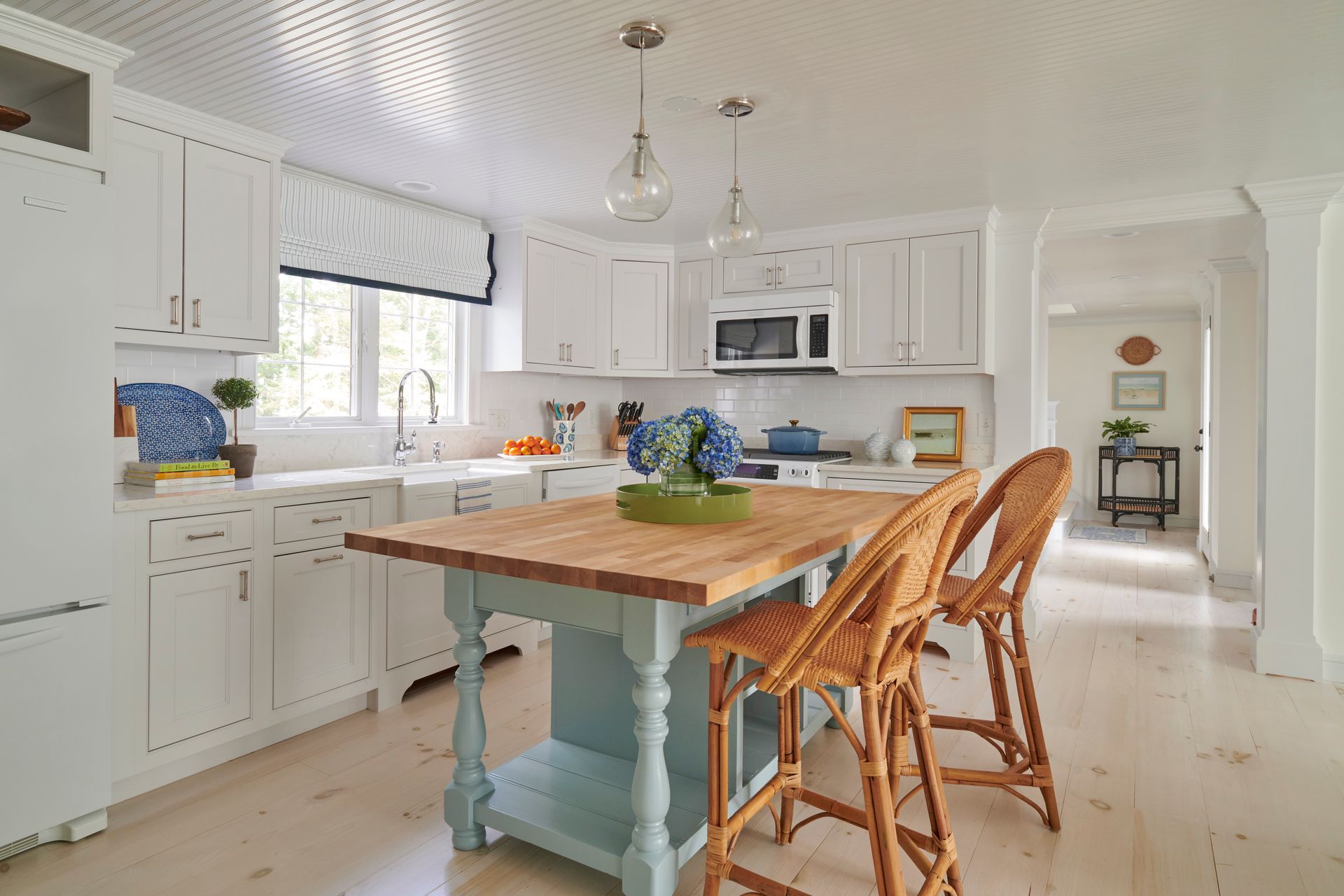 A kitchen with white cabinets, a wooden table, and wicker chairs