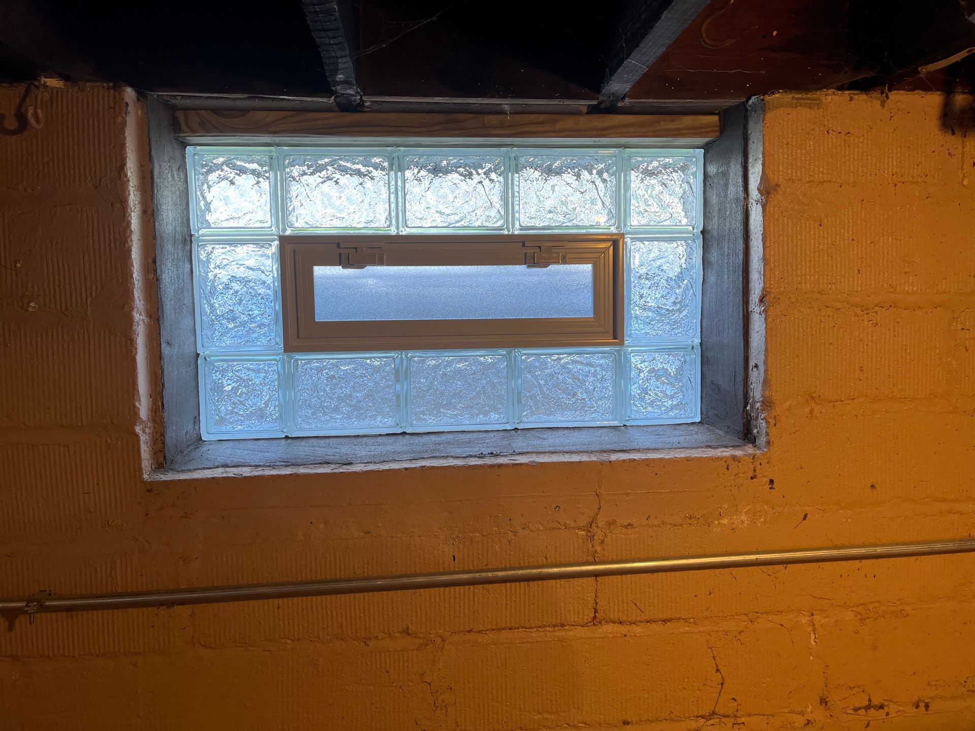 Glass block window in a basement wall with a small, central window.