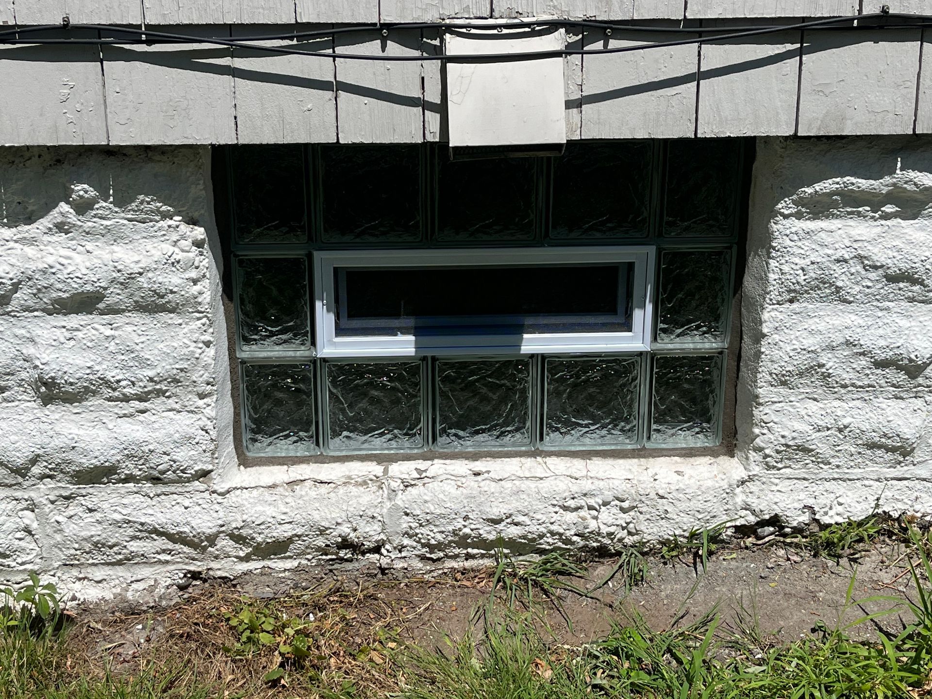 Basement window made of glass blocks in a white stone wall.