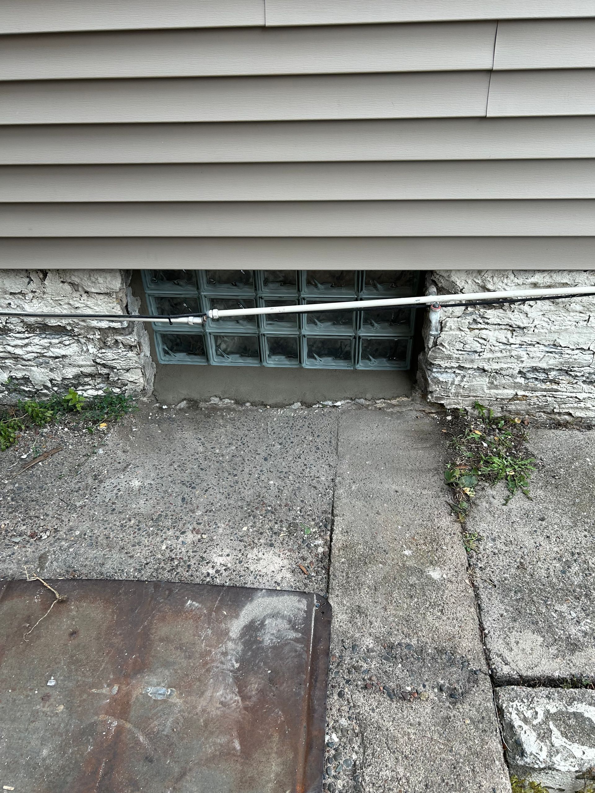 Exterior view of a building with a glass block basement window, concrete steps, and siding.