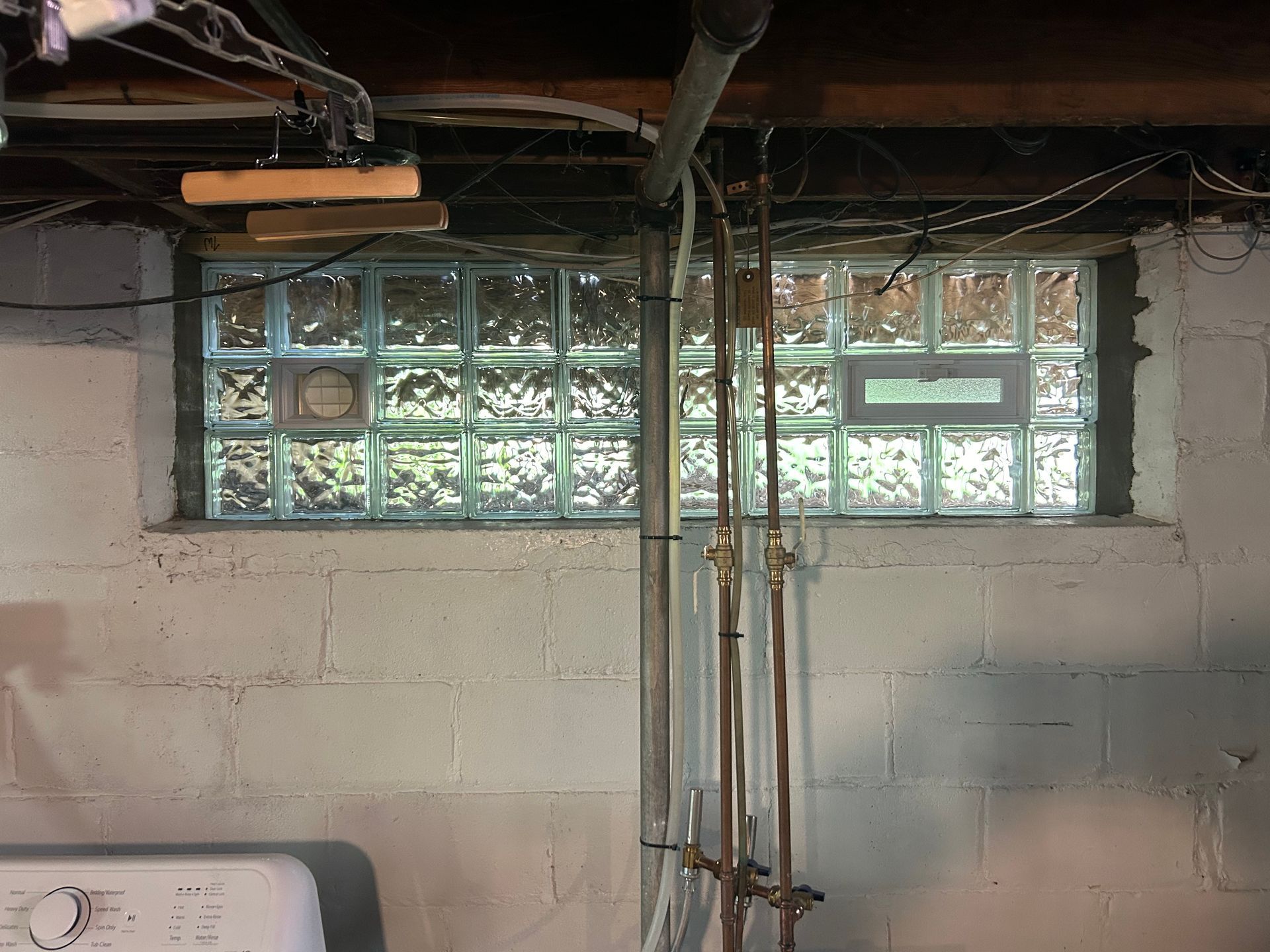 Basement interior with glass block windows, white walls, pipes, and a washing machine.