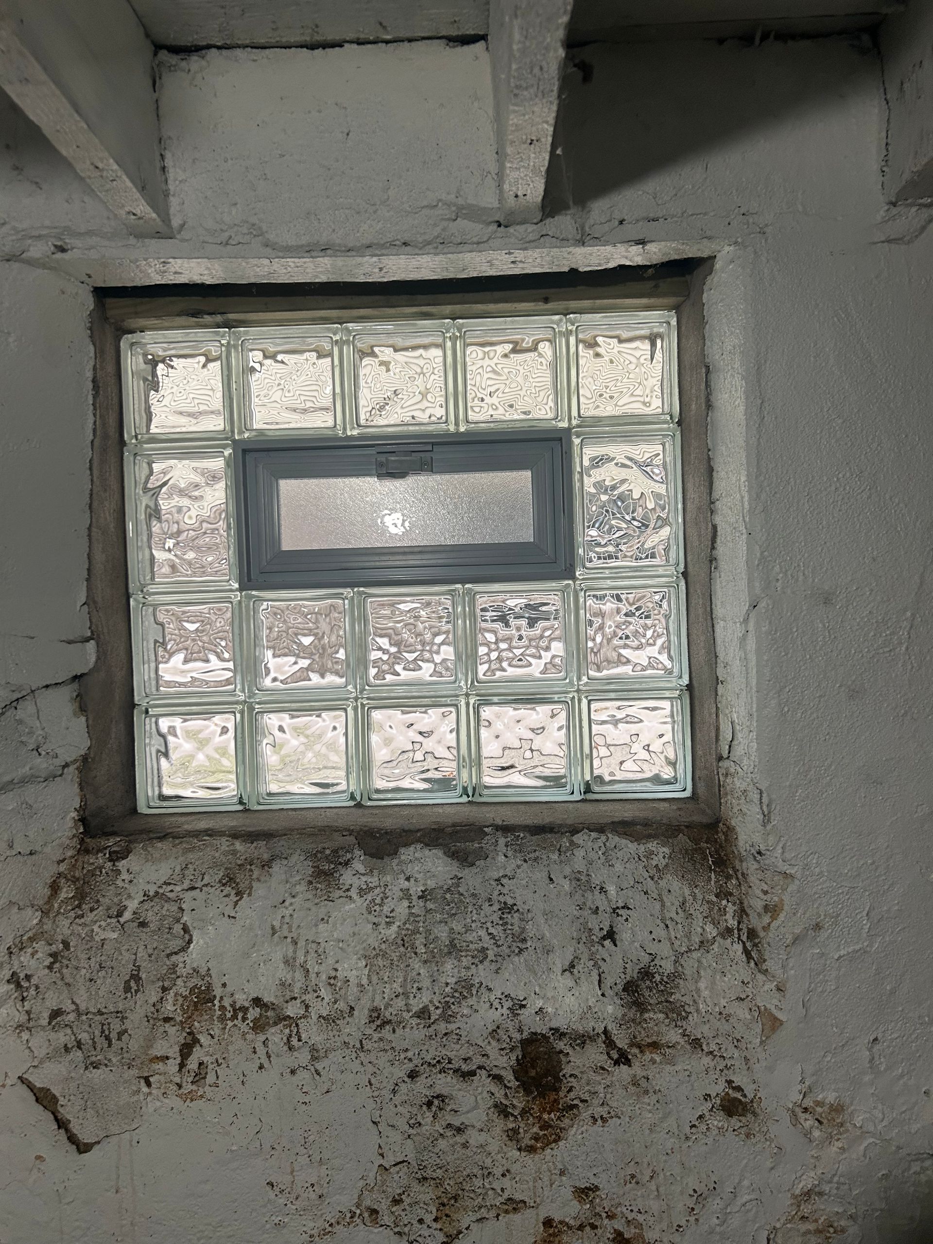 Glass block window in a concrete wall. Central rectangular vent. Old, stained wall.