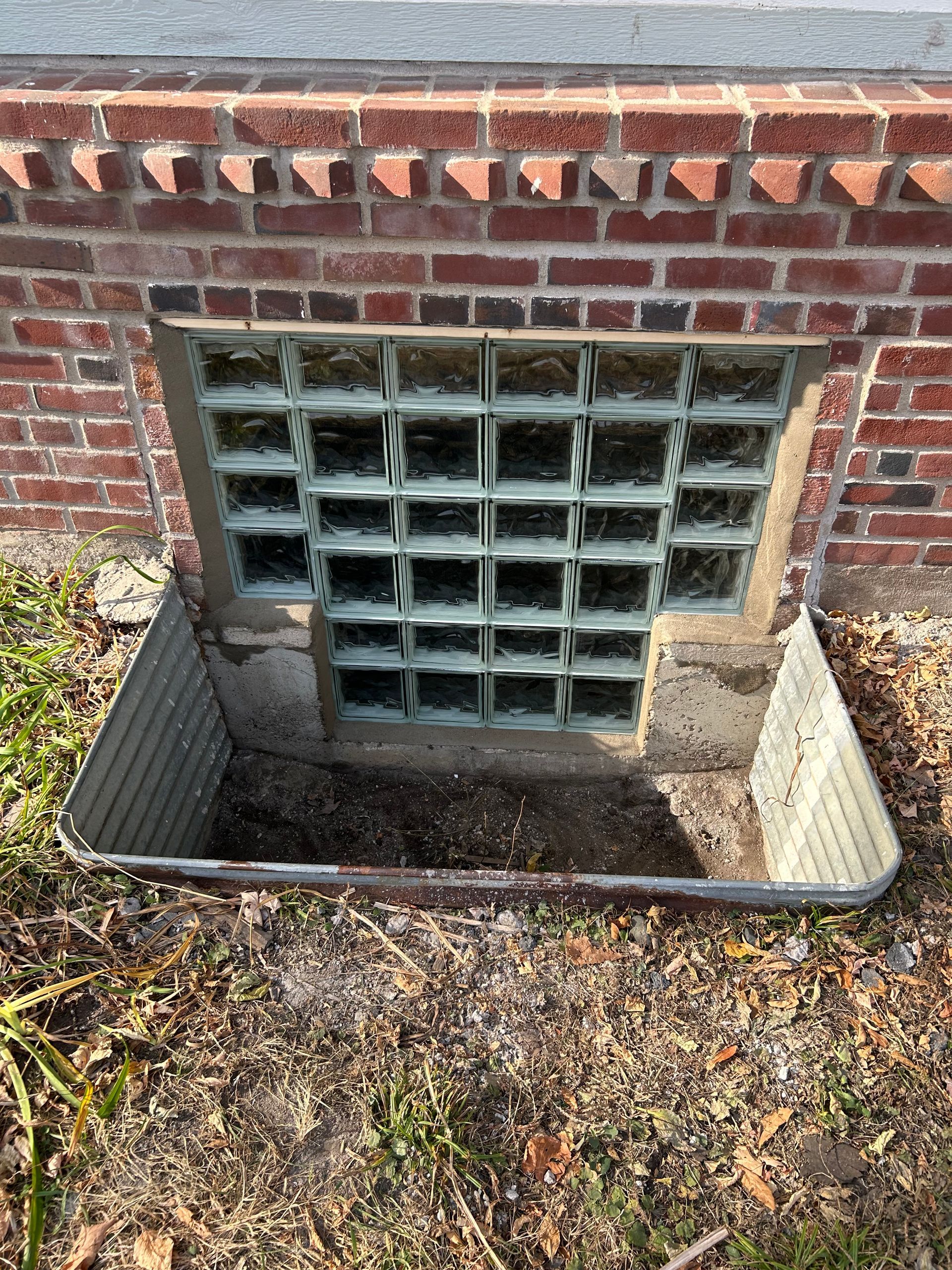 Brick building with a glass block window above a metal window well.