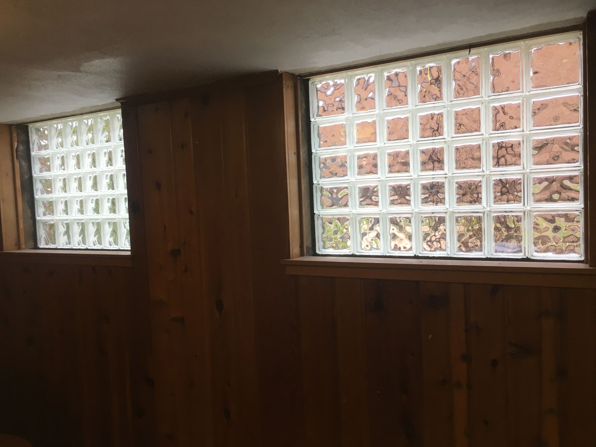 Two basement glass block windows in wood paneled room, providing light and ventilation.