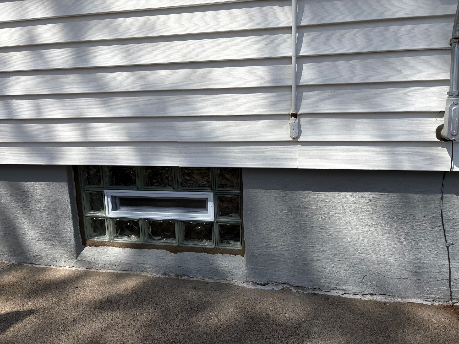 White siding above a gray concrete foundation with a rectangular glass block window.