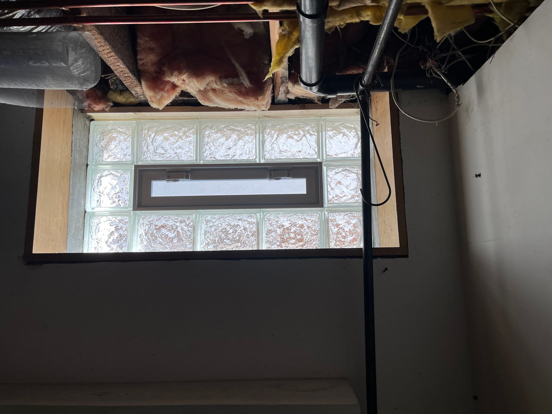 Basement window with glass blocks and a small window. Exposed ceiling with insulation.