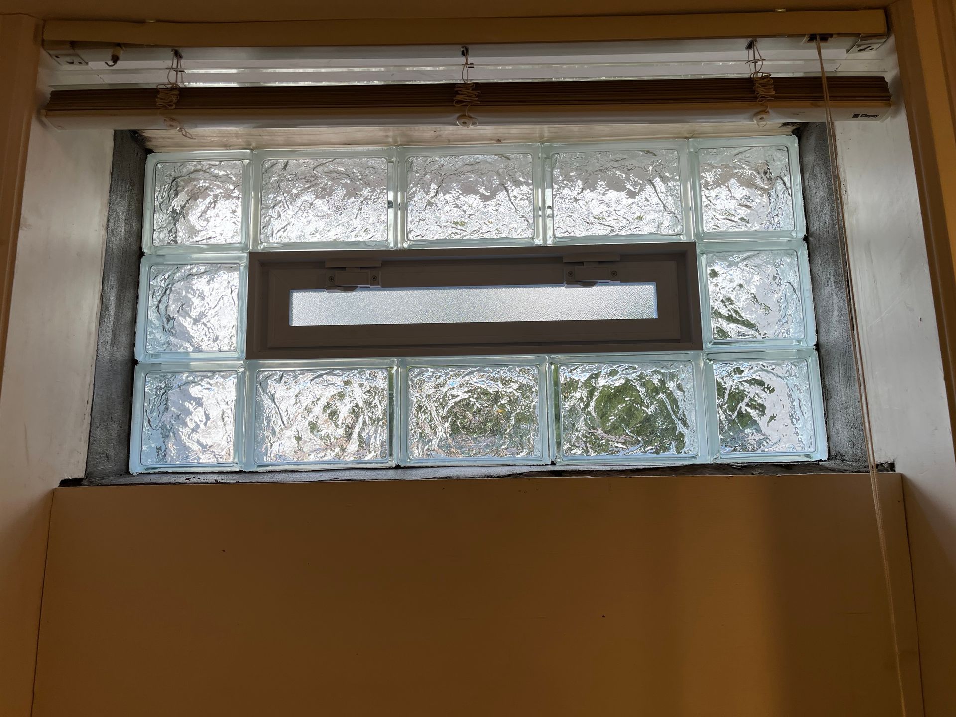 Glass block window with a small, rectangular window in the middle; in a beige wall.