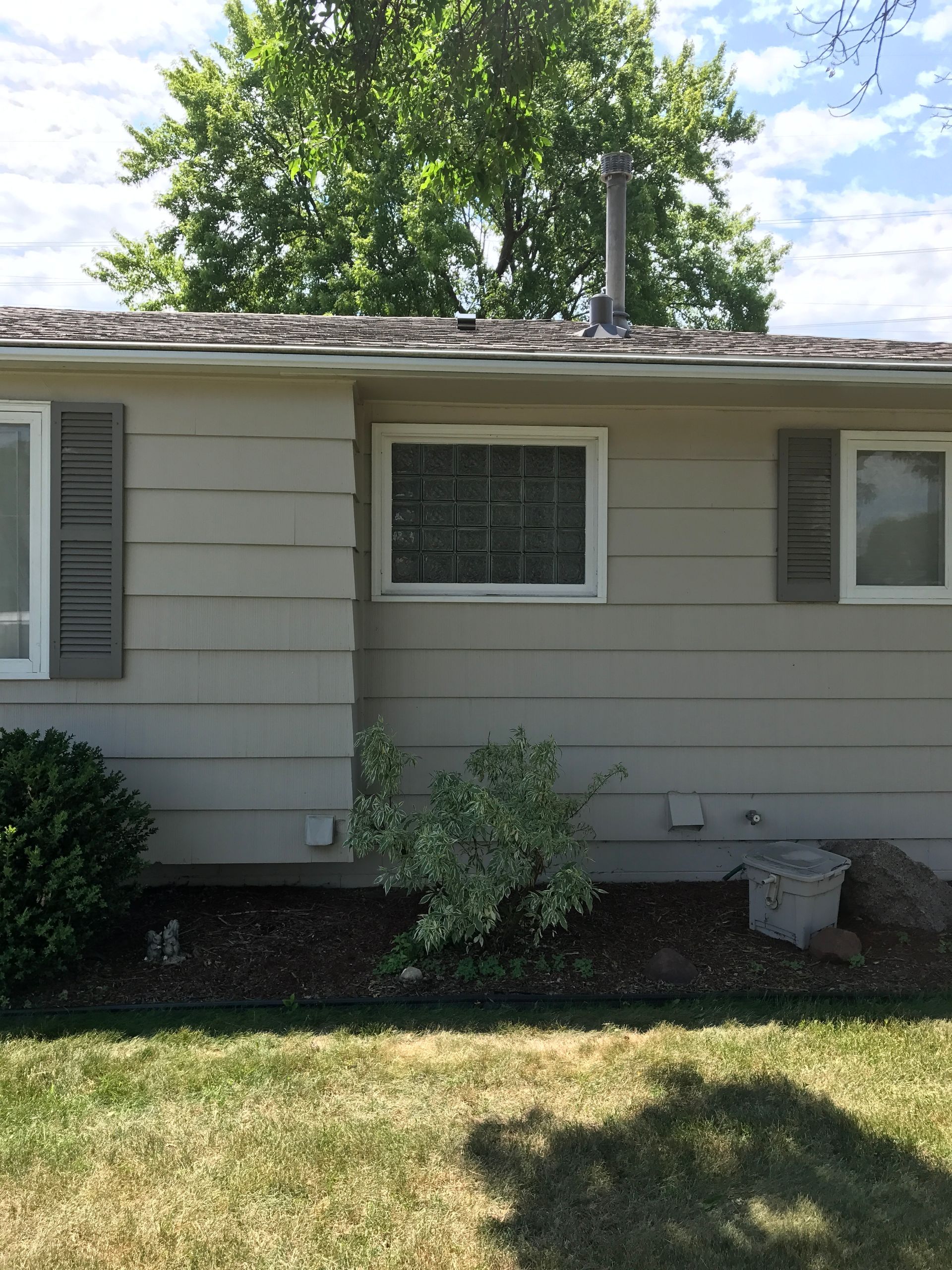 Beige house with gray shutters and a glass block window, against a green grassy backdrop.