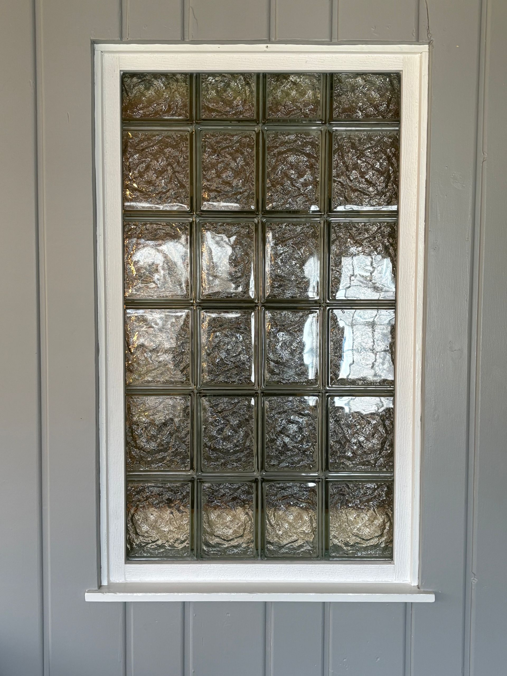Glass block window set in white frame on gray wall.