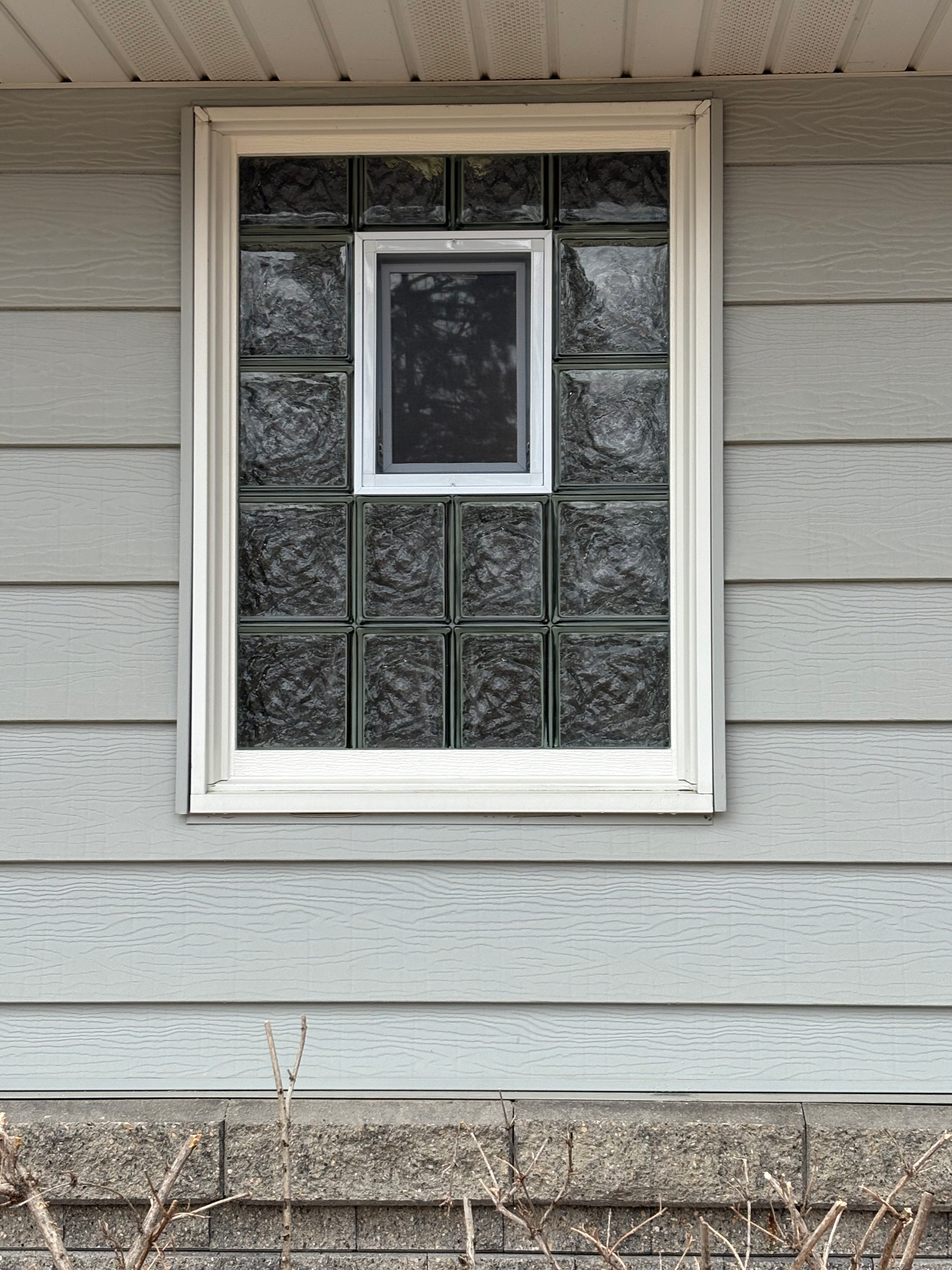 Window with small central window, surrounded by glass blocks, on a gray house exterior.