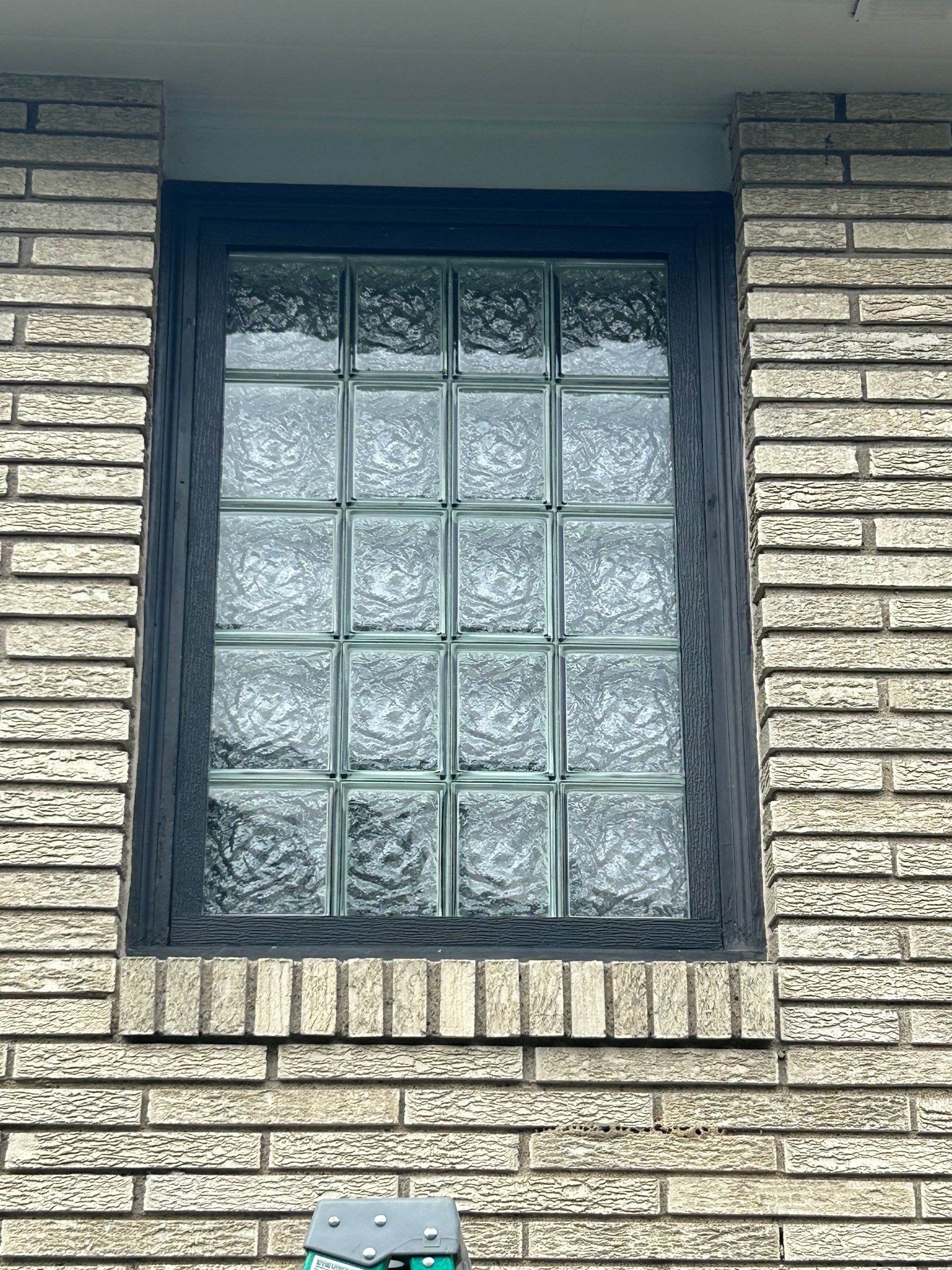 Window made of glass blocks in a brick wall, framed with black trim.