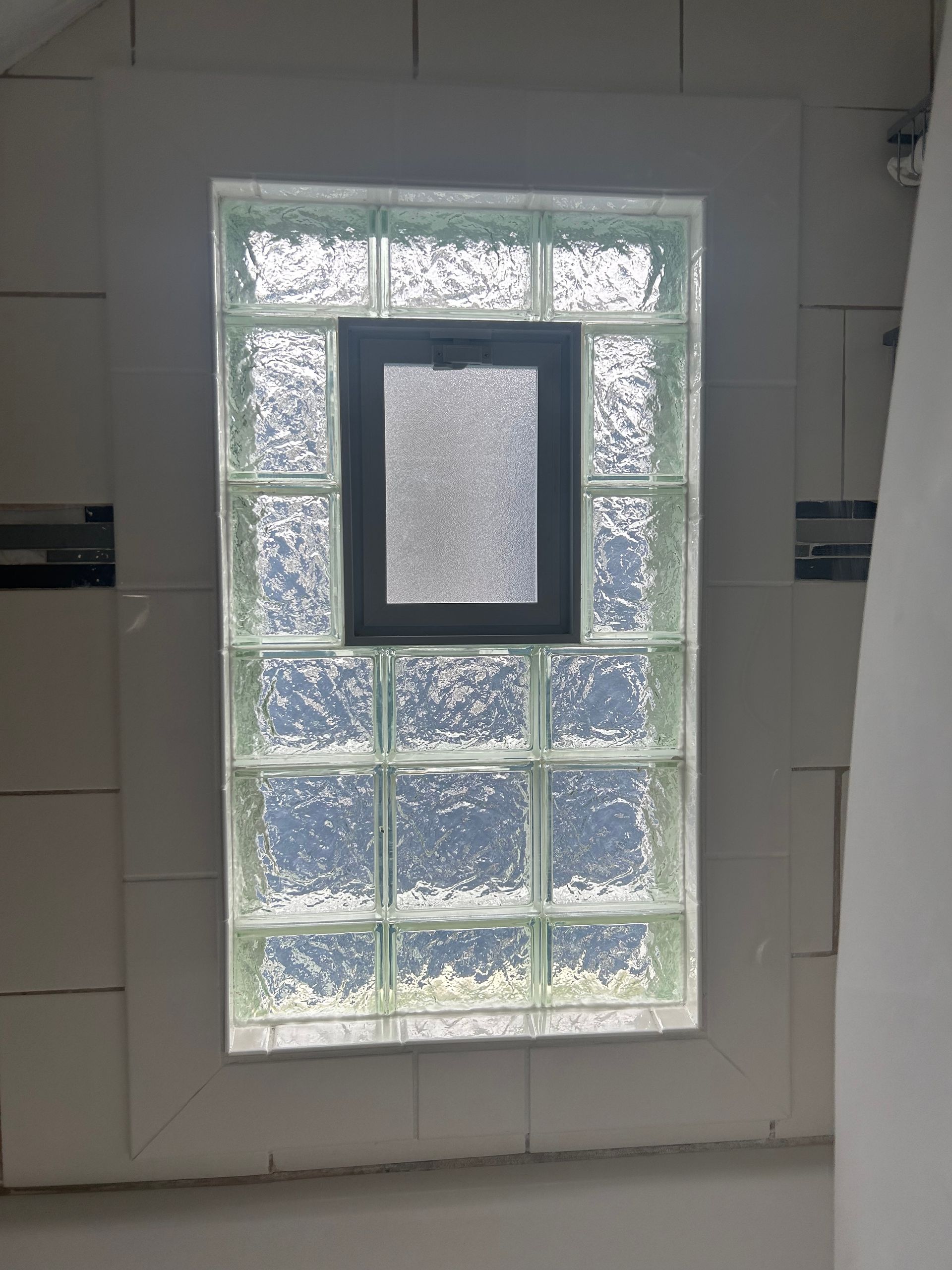 Glass block window with a small, dark window centered. White tiled wall.