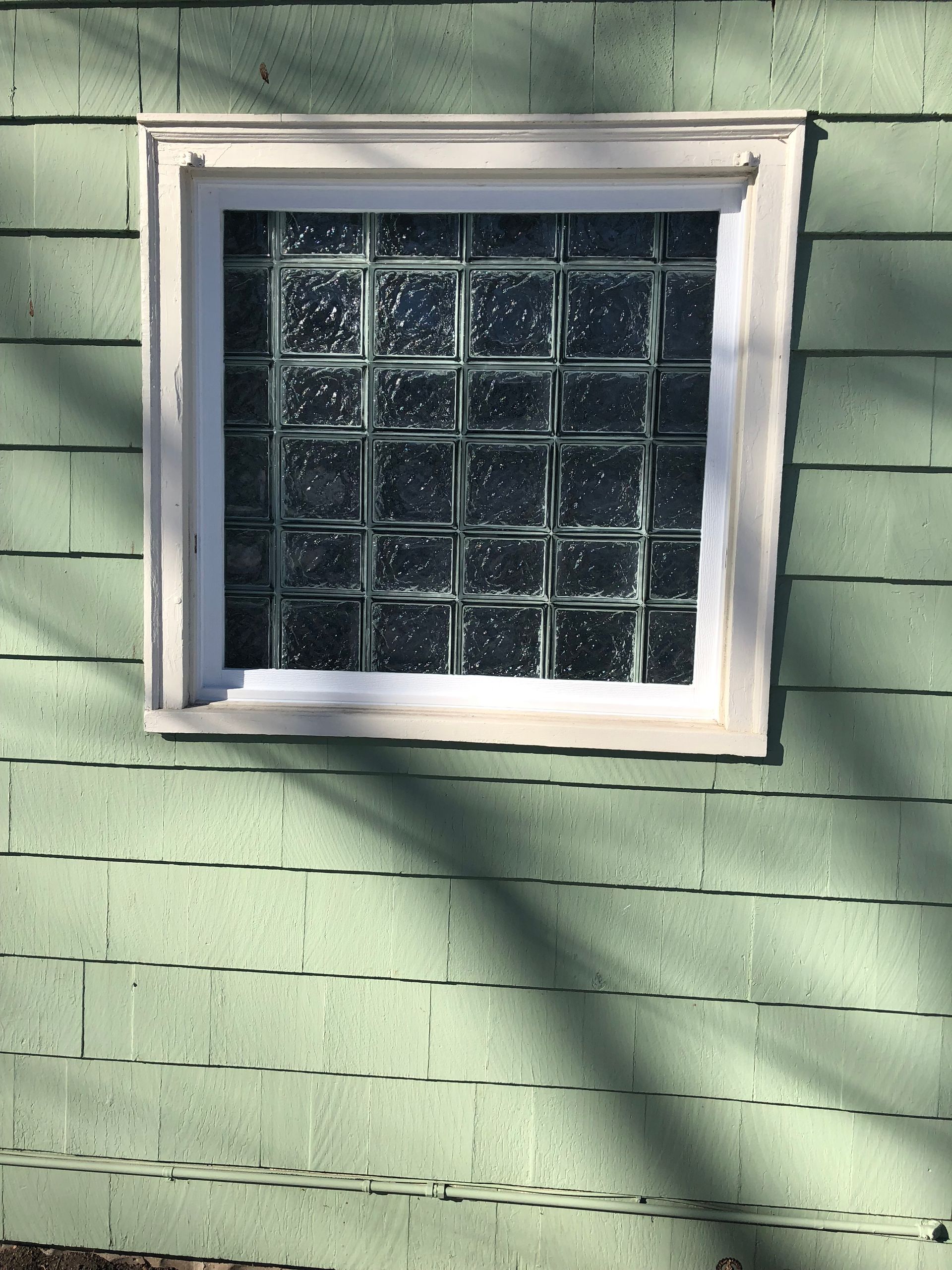 Square glass block window in a white frame set in green siding.